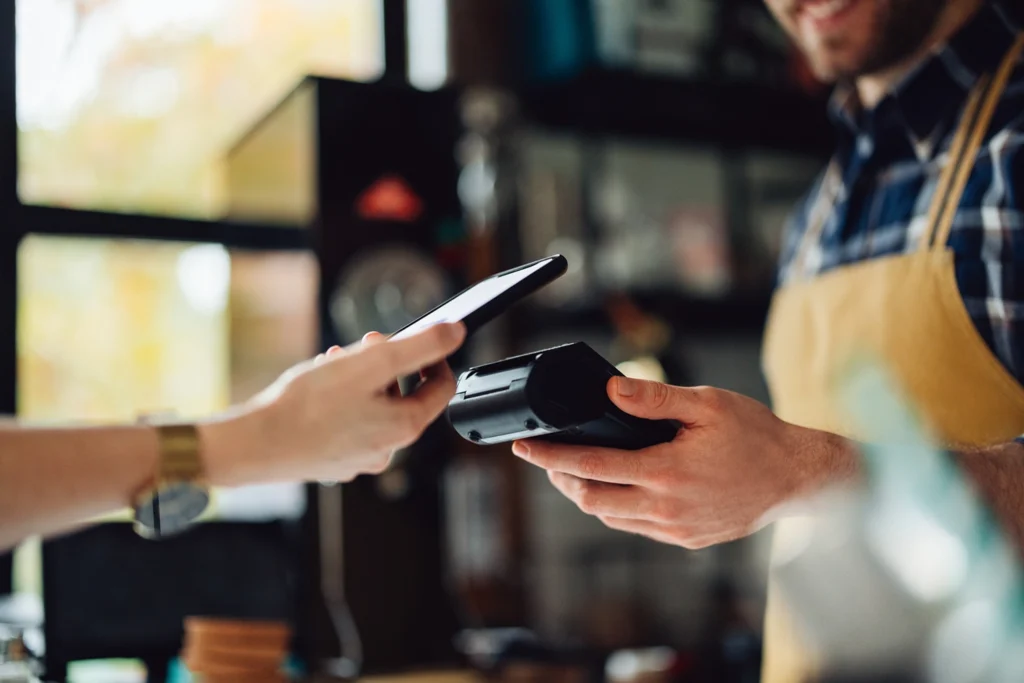 Country-Bank-customer-holding-up-phone-to-card-reader-at-business-establishment