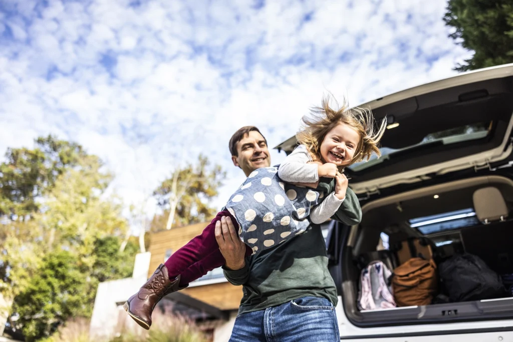 Country-Bank-man-holding-daughter-near-trunk-of-packed-car