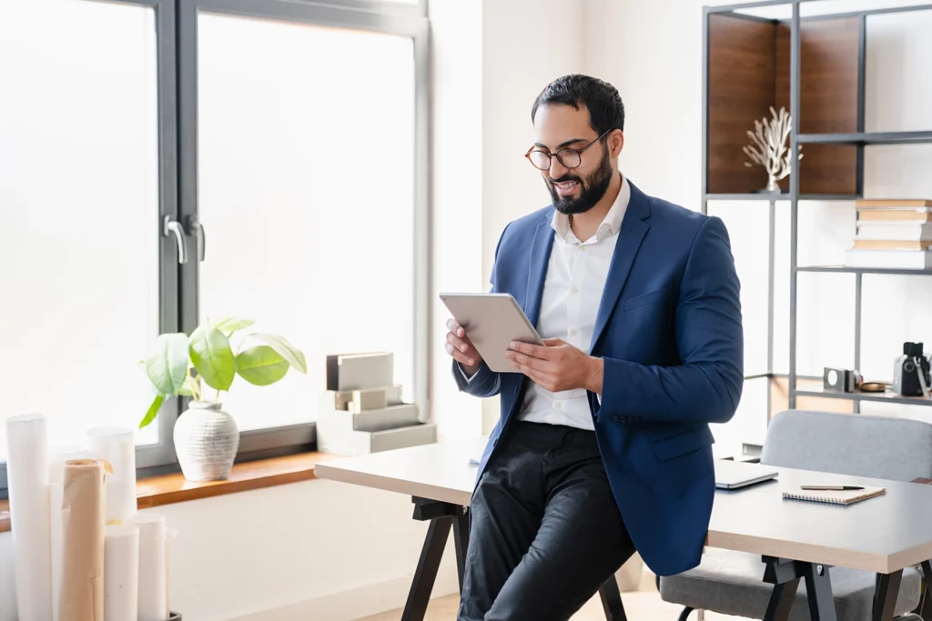 Country-Bank-man-holding-tablet-while-leaning-against-his-office-desk