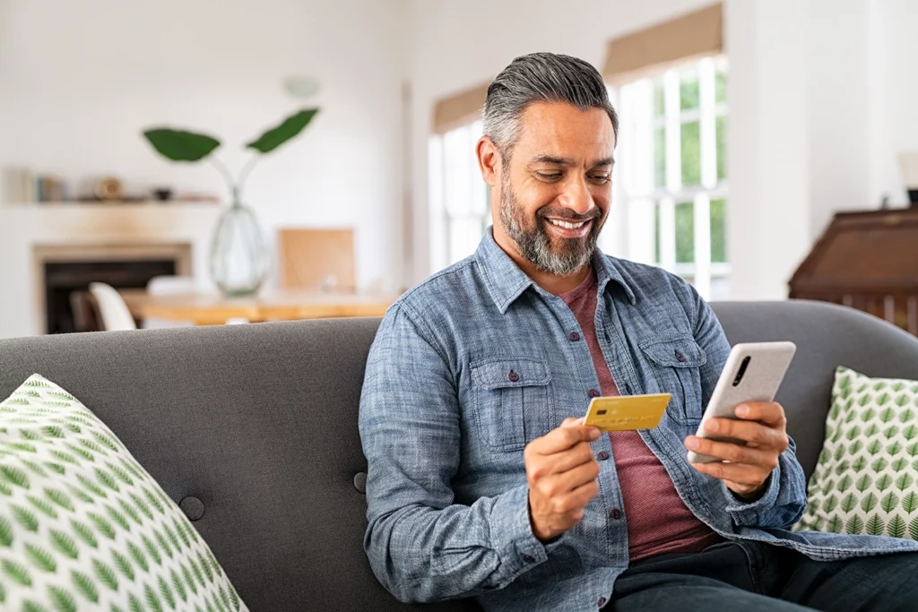 Country-Bank-man-smiling-while-holding-his-debit-card-and-shopping-from-his-phone