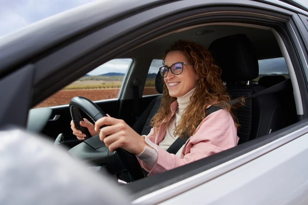Country-Bank-smiling-woman-wearing-blue-glasses-pink-sweater-driving-a-car