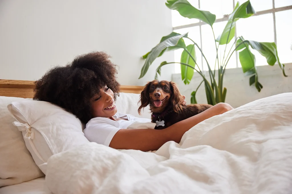 CountryBank-woman-laying-in-white-bed-holding-onto-her-brown-dog